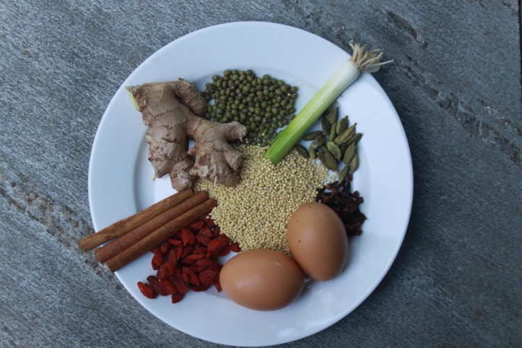 Clockwise from top: Mung Beans, Green Onion, Cardamom seeds, clove, eggs, goji berries, cinnamon sticks, fresh ginger root and millet in the middle.